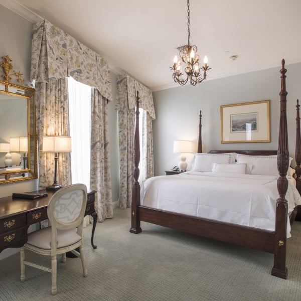 Superior King room featuring a dark wood four-poster bed, a writing desk with a gold mirror, and patterned curtains.