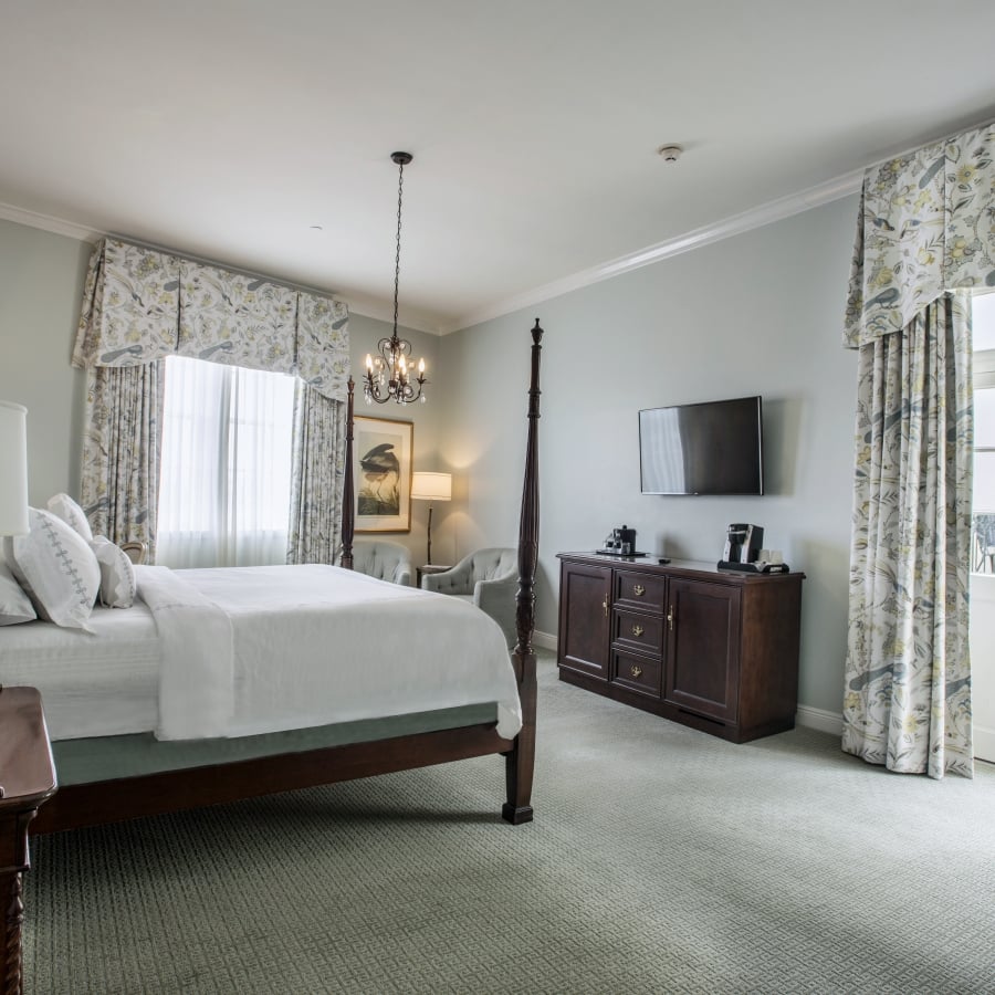 Superior King room with a dark wood four-poster bed, light blue-green walls, floral/bird-patterned curtains, and an open door to a small balcony.