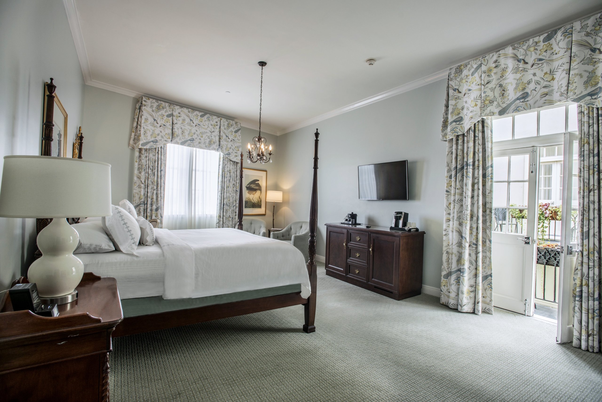 Superior King room with a dark wood four-poster bed, light blue-green walls, floral/bird-patterned curtains, and an open door to a small balcony.