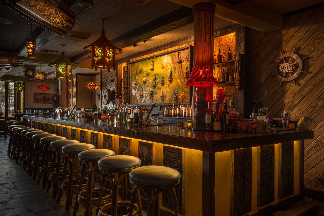 The dark, atmospheric interior of a tiki bar (Latitude 29), featuring a glowing bar counter and bamboo stools.