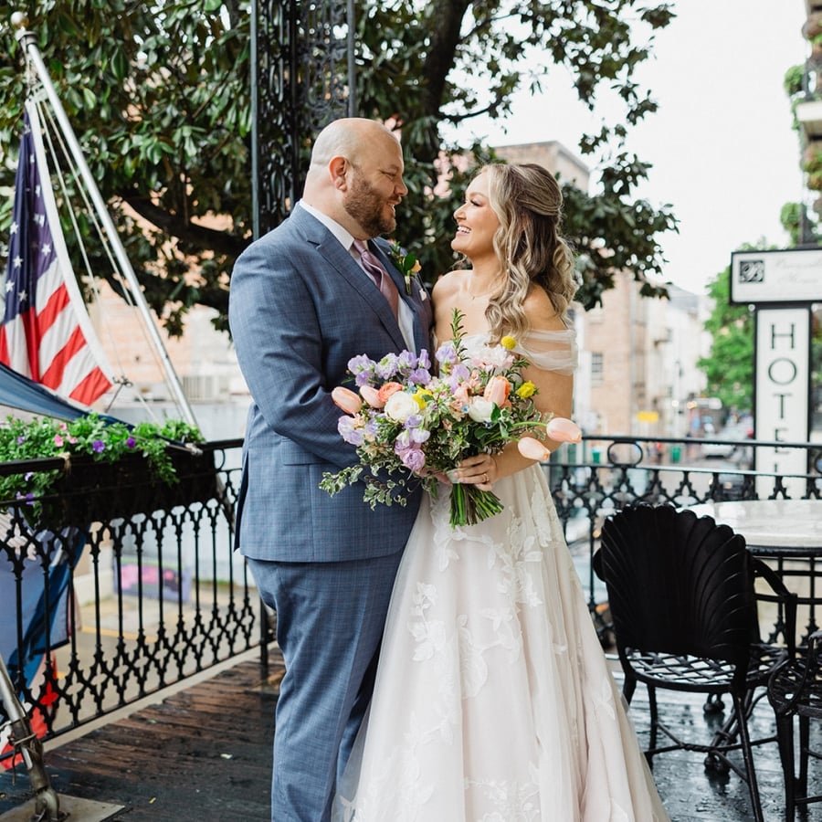 A bride and groom look into each other's eyes, embracing on an outdoor wrought-iron balcony.