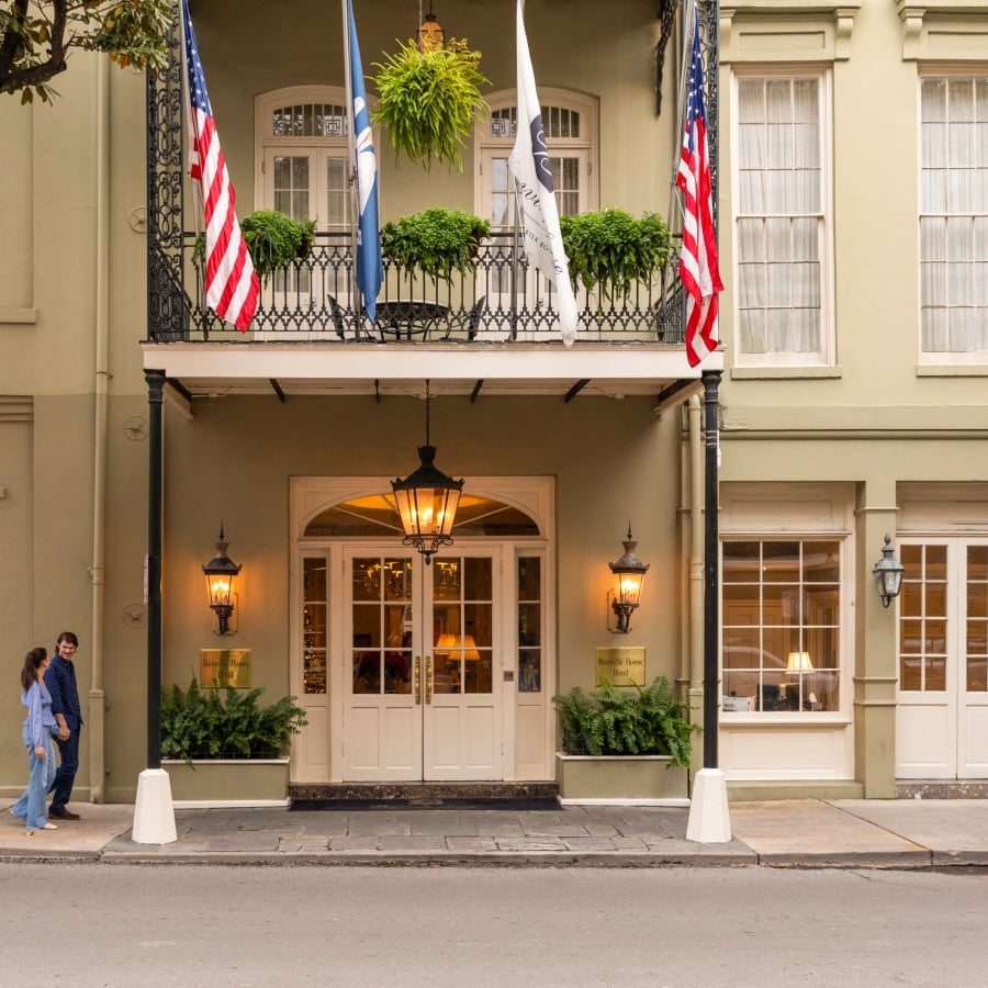 The elegant Bienville House Hotel entrance with flags, wrought-iron balcony, and a couple standing nearby.