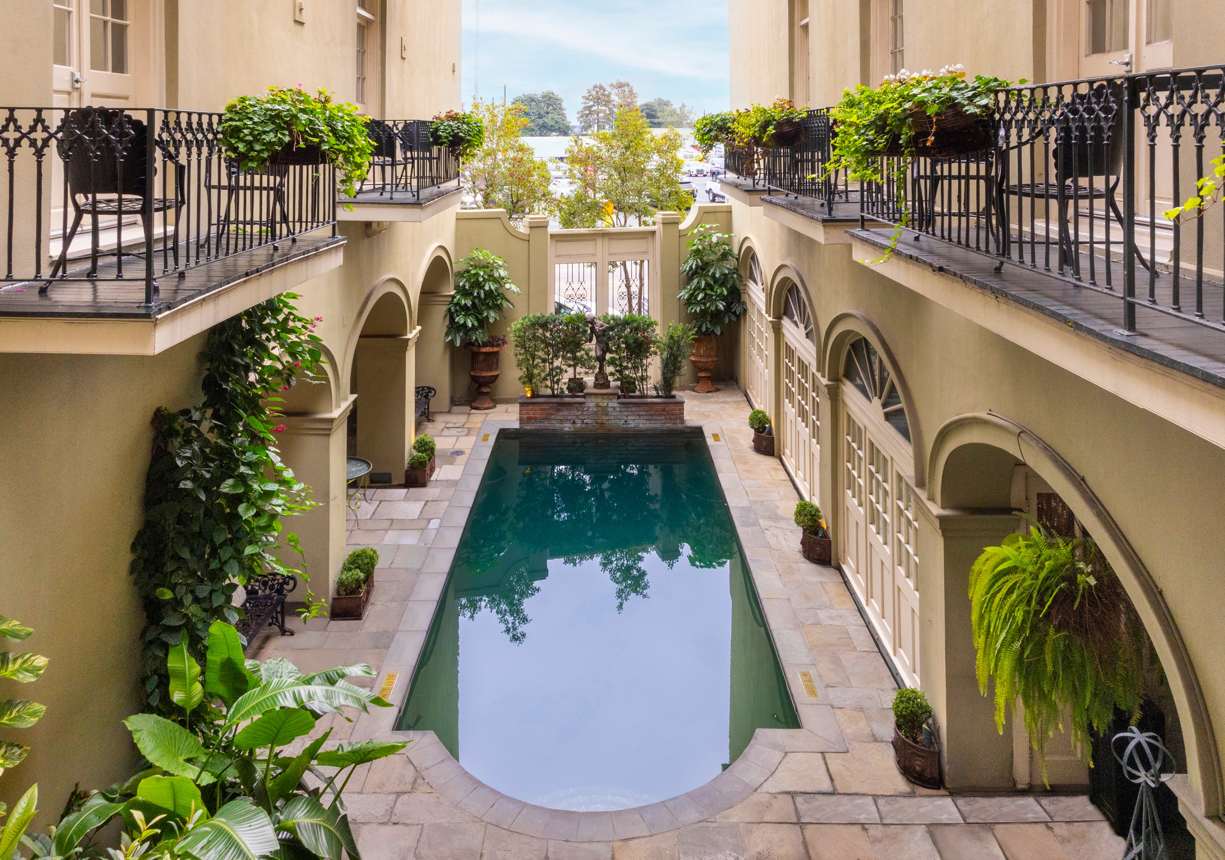 A serene pool area surrounded by beige walls, balconies, and lush greenery.