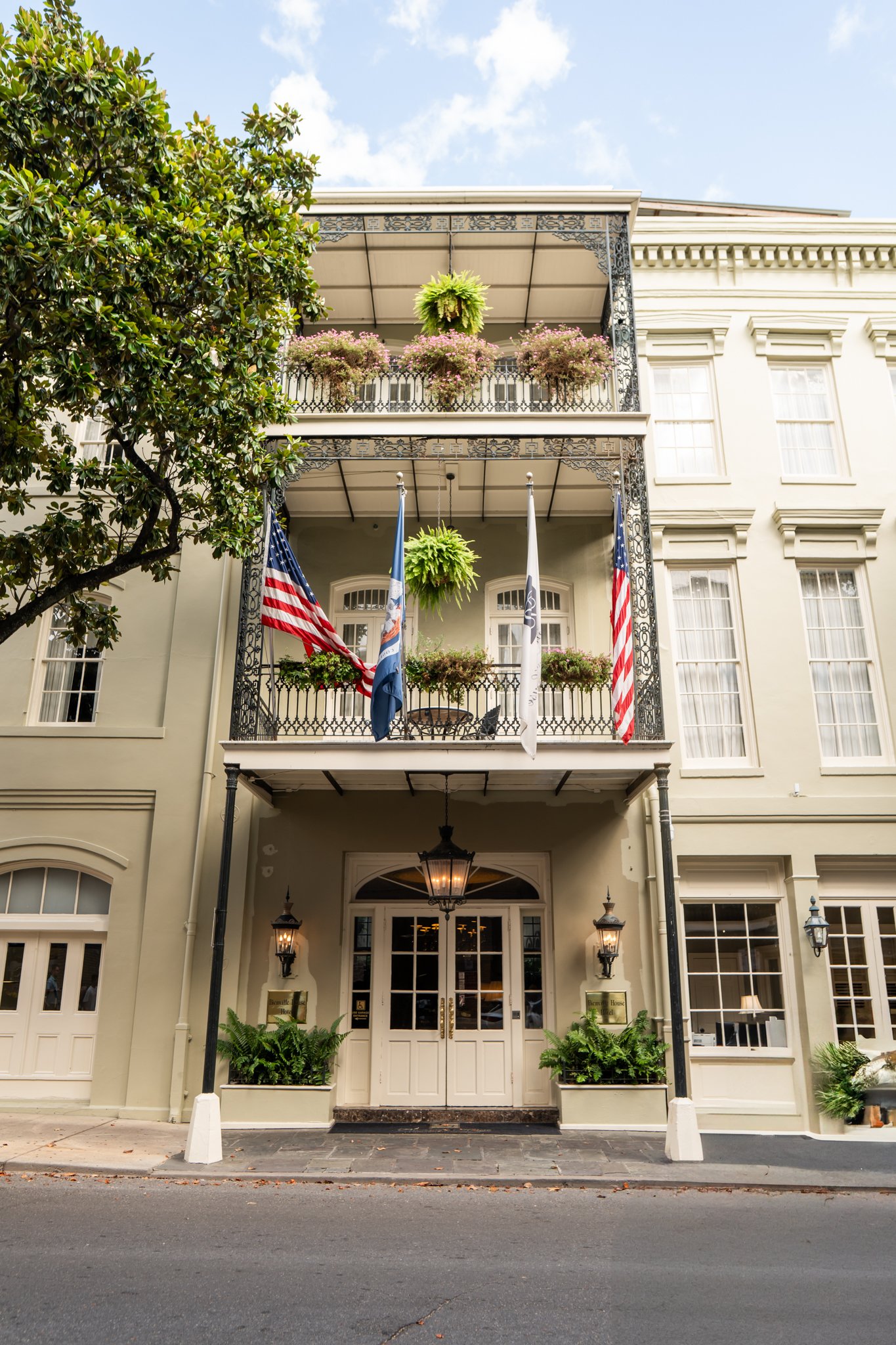 The Bienville House Hotel exterior entrance, featuring two levels of wrought-iron balconies and flags.