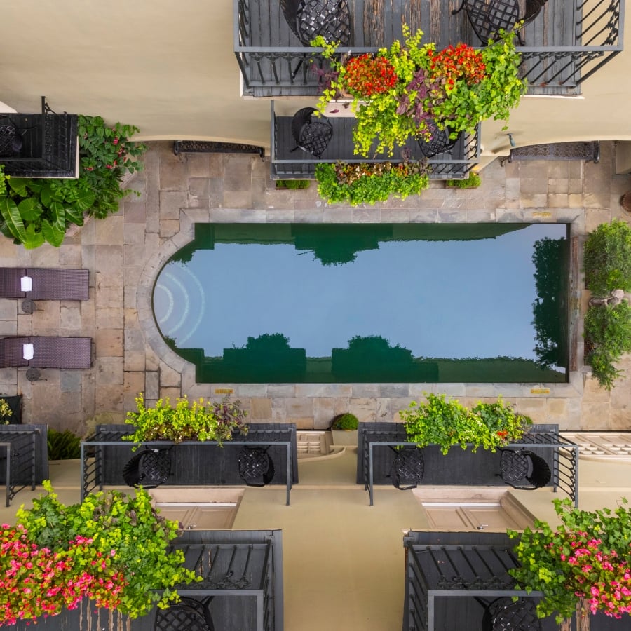 A top-down aerial view of the hotel's courtyard pool, surrounded by black balconies and planters with flowers.