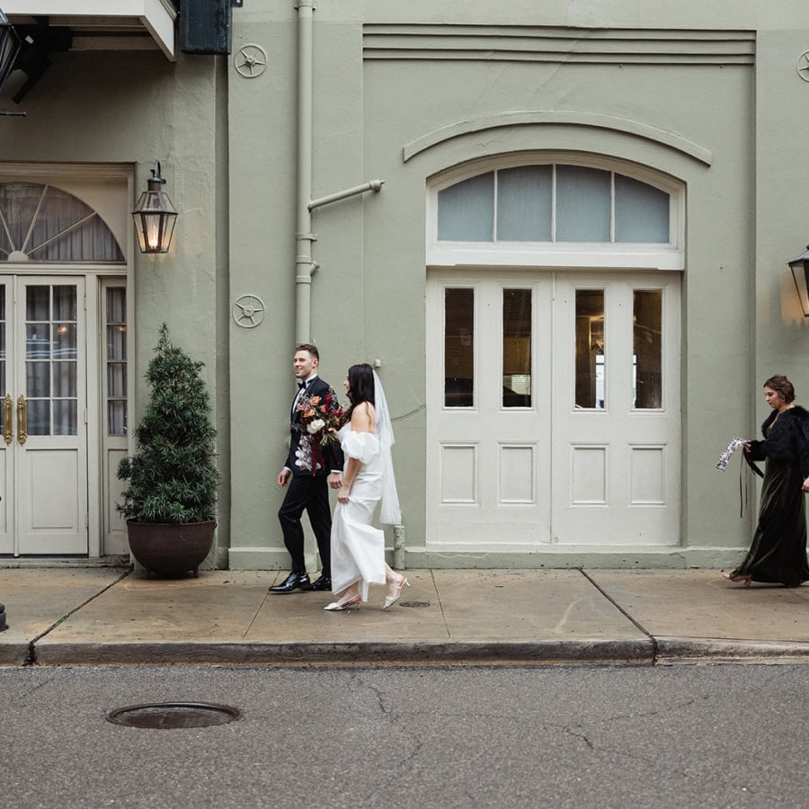 The bride and groom walk hand-in-hand down a city sidewalk after their wedding ceremony.