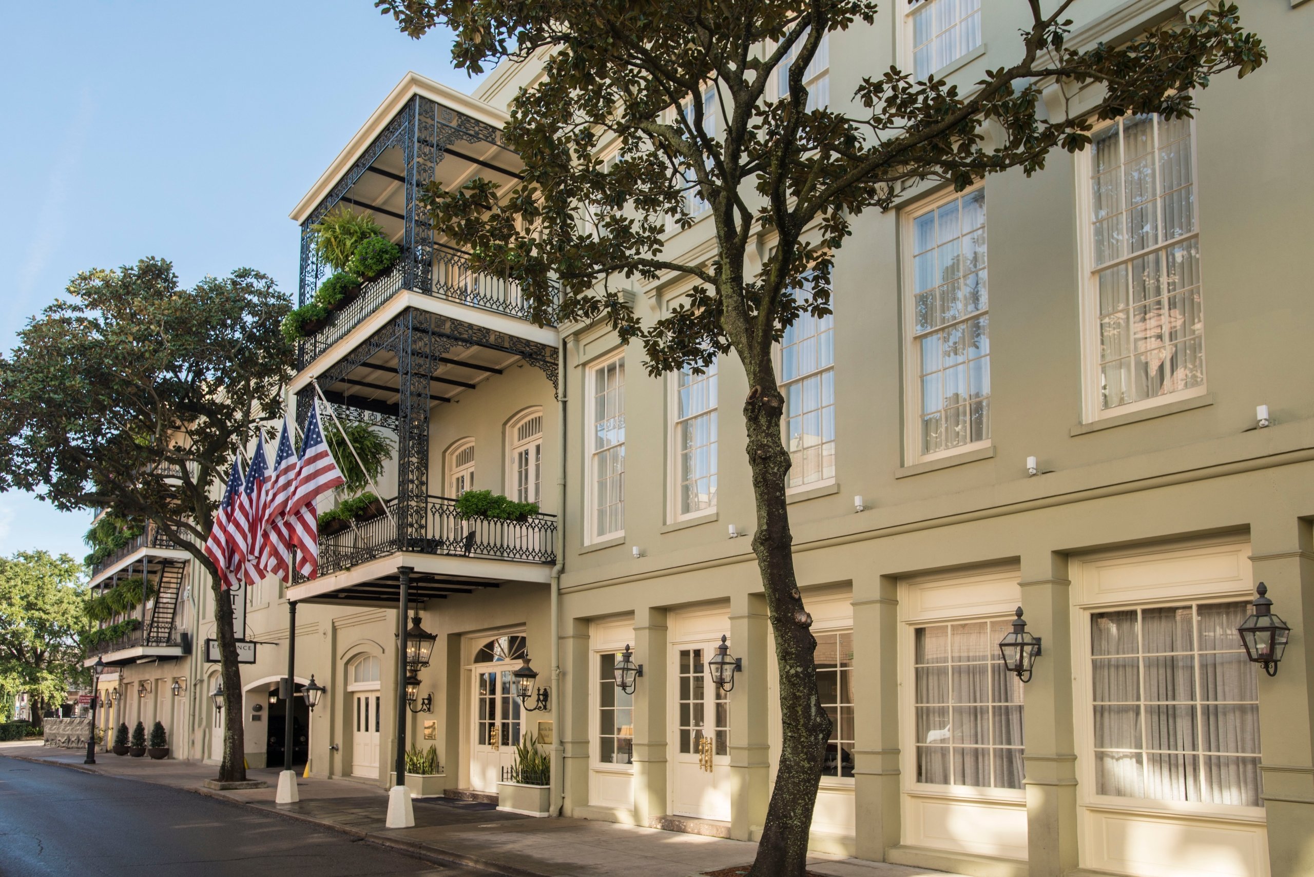 The Bienville House Hotel facade with its iconic wrought-iron balcony and three American flags hanging at the entrance.