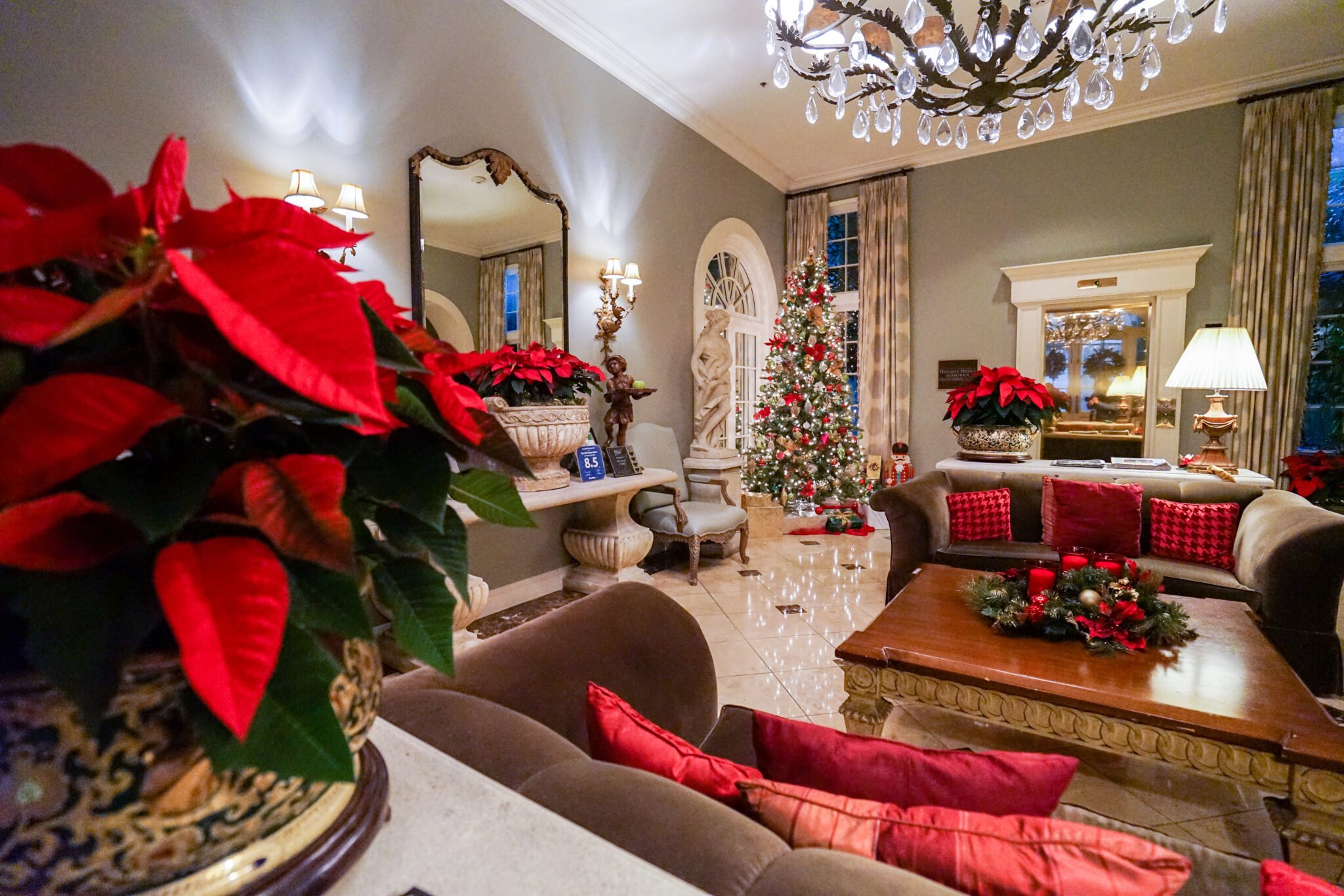 The Bienville House hotel lobby decorated for Christmas, featuring red poinsettias, velvet sofas, and a lighted Christmas tree.