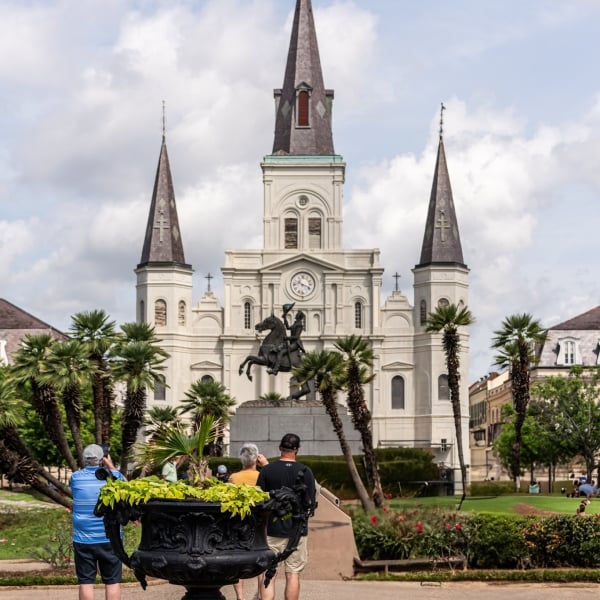 View of St. Louis Cathedral in Jackson Square, New Orleans, with a statue of Andrew Jackson, palm trees, and tourists in the foreground.