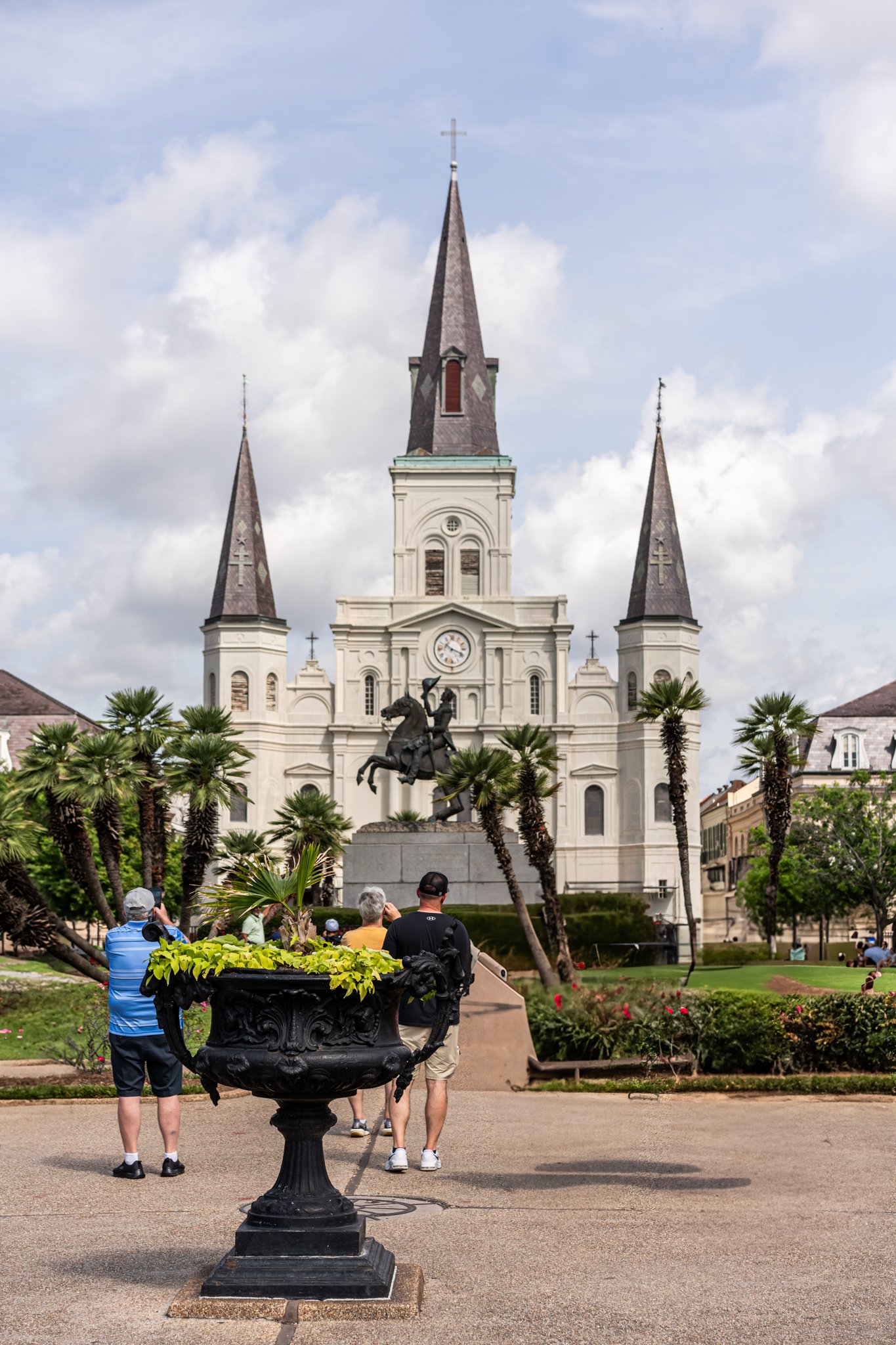View of St. Louis Cathedral in Jackson Square, New Orleans, with a statue of Andrew Jackson, palm trees, and tourists in the foreground.
