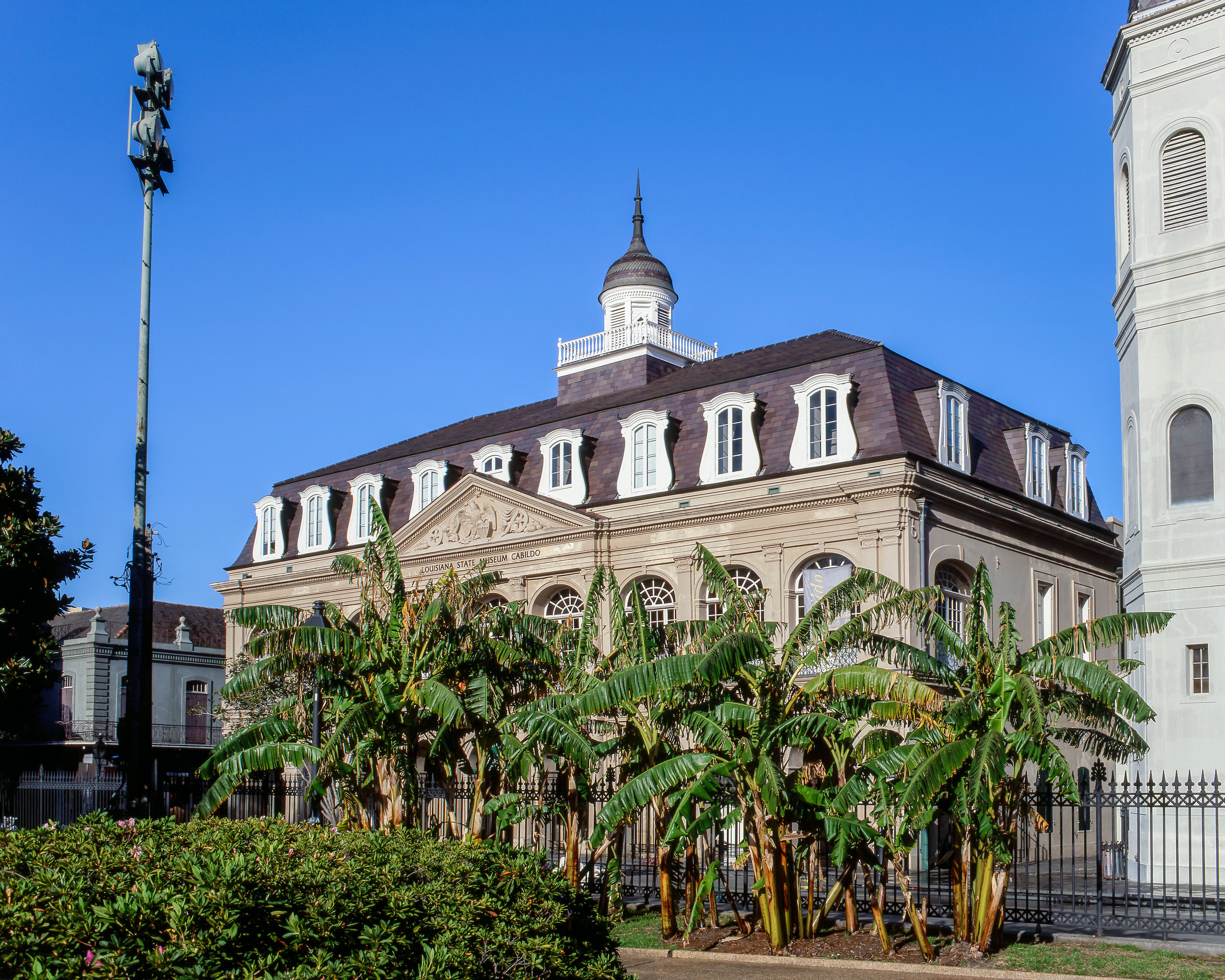 A large building with a brown roof and white trim, surrounded by trees and a fence.