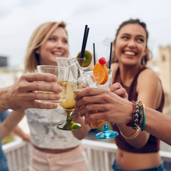 Friends having fun and drinking cocktails outdoor on a rooftop get together. Group of friends hanging out and toasting drinks outdoors. Focus on glasses.