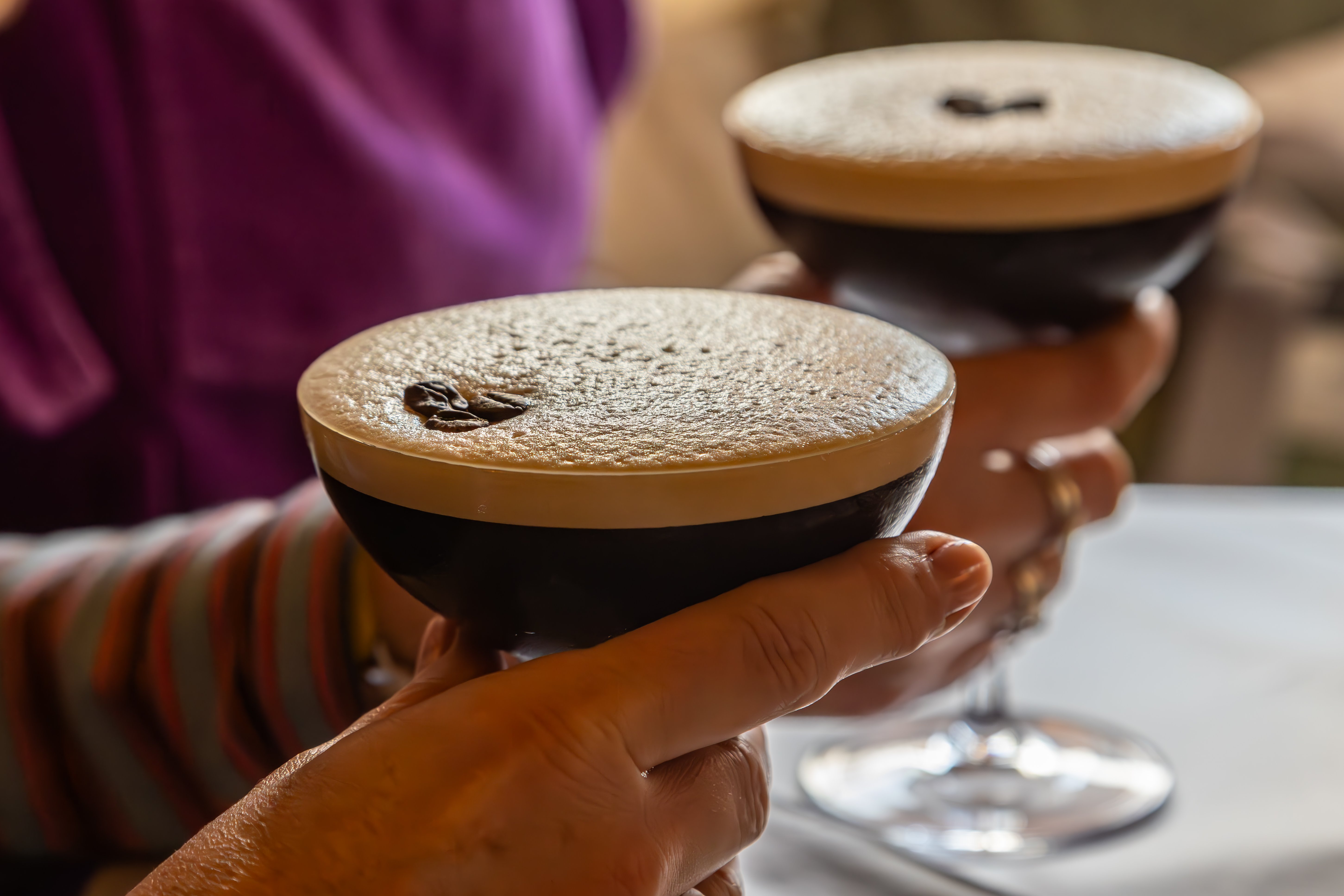 Two hands holding coffee drinks with a thick layer of foam on top.