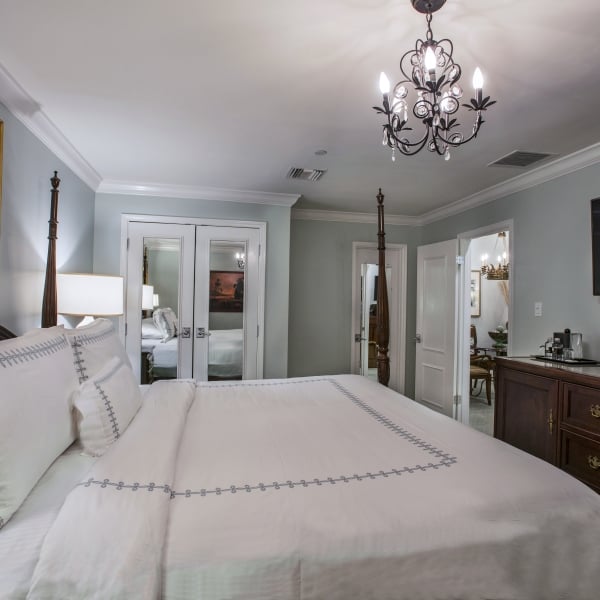 Luxury hotel bedroom with a dark wood four-poster king bed, white bedding, nightstands, and a mirrored closet reflecting the room.