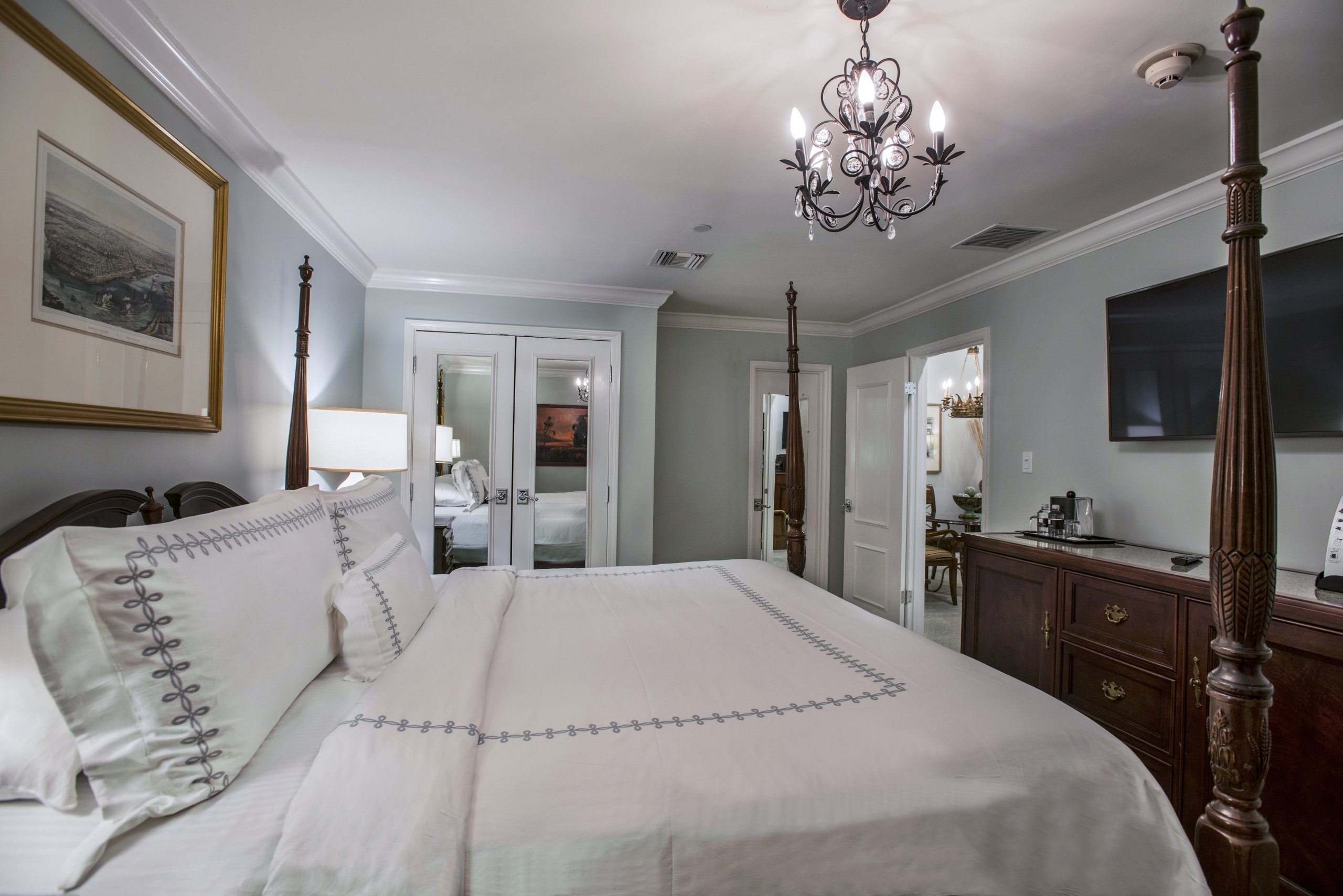 Luxury hotel bedroom with a dark wood four-poster king bed, white bedding, nightstands, and a mirrored closet reflecting the room.