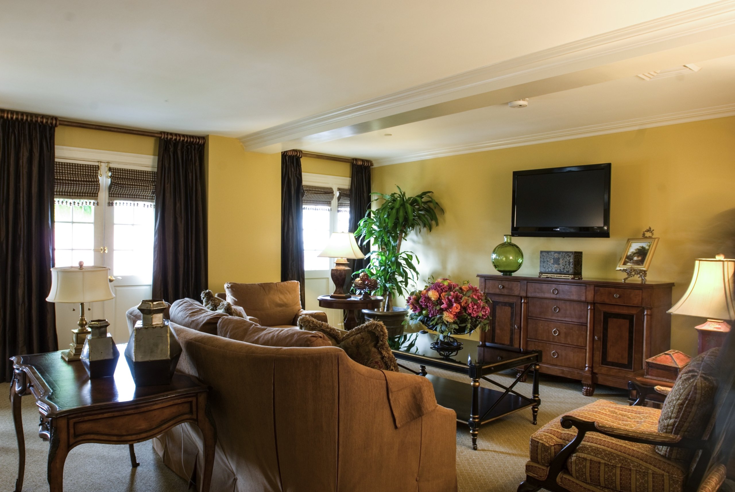 Penthouse suite living room with yellow walls, a tan sofa, dark wood furniture, and a flat-screen TV above a buffet cabinet.