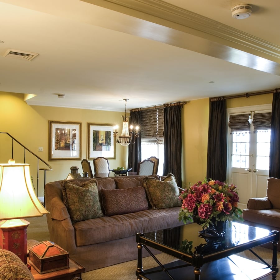 Penthouse suite living room looking toward the dining area and staircase, with a brown patterned sofa and tiered ceiling.