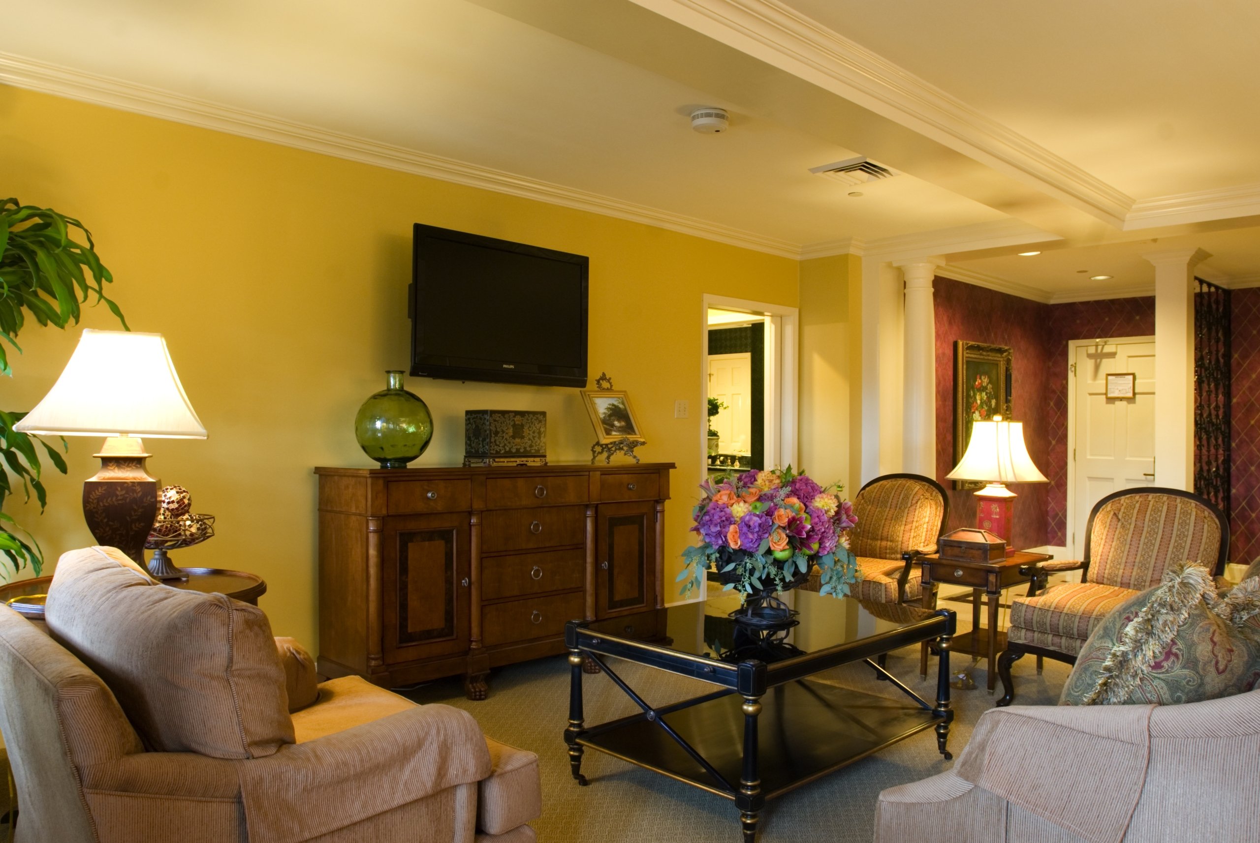 Close-up of the Penthouse Suite living room entertainment area with a TV, dark wood cabinet, and two striped chairs near an entryway.