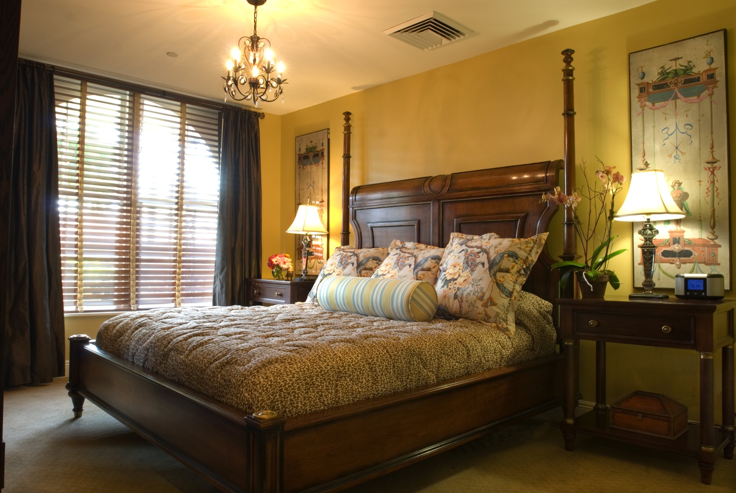 King-sized dark wood sleigh bed with leopard-print and floral bedding, yellow walls, and a chandelier in the penthouse suite bedroom.