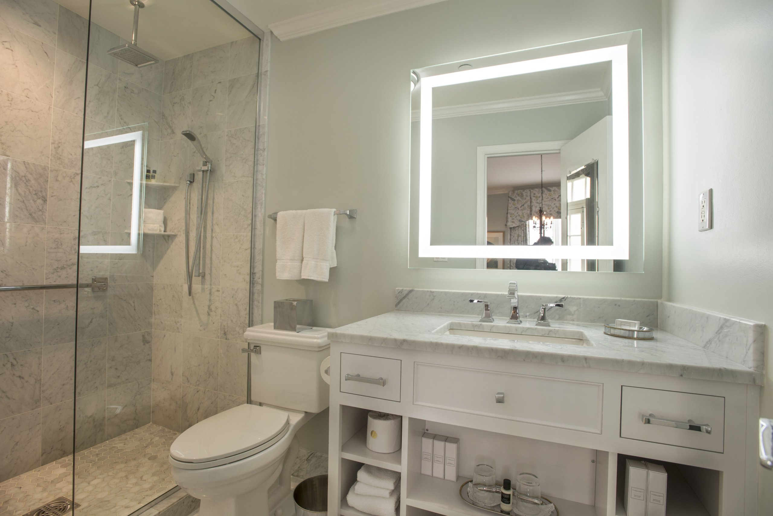 Renovated bathroom with a white marble vanity, sink, toilet, and a glass-enclosed shower with subway and hexagon marble tiling.