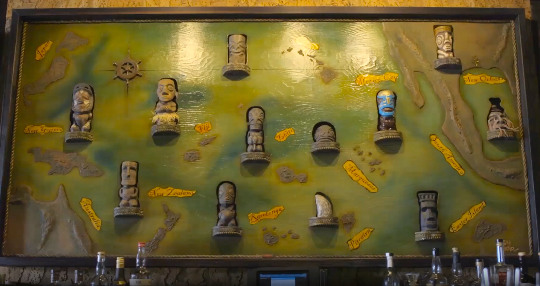 A large wooden map artwork with raised relief and carved tiki figures, marking various locations worldwide.