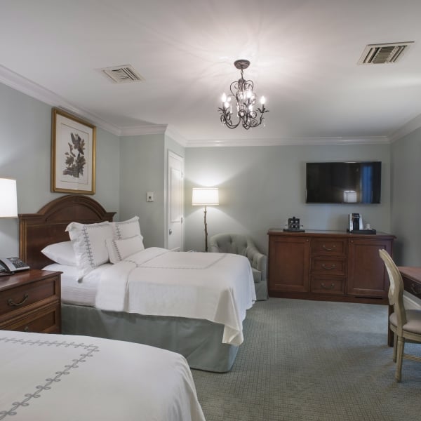 A hotel room with two beds, light blue walls, dark wood furniture, and a chandelier.
