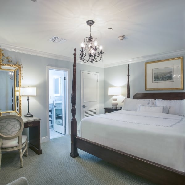 Standard King room showing the bed, a dark wood desk with a gold mirror, and an open doorway to a marble bathroom.