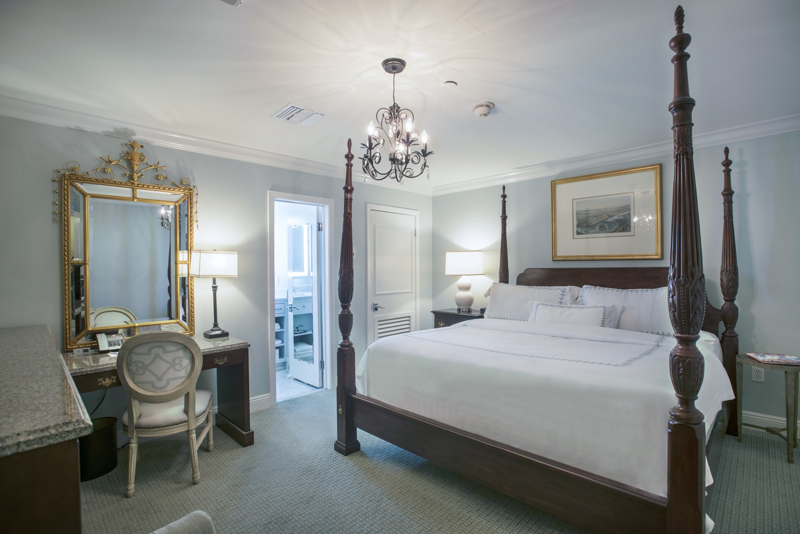 Standard King room showing the bed, a dark wood desk with a gold mirror, and an open doorway to a marble bathroom.