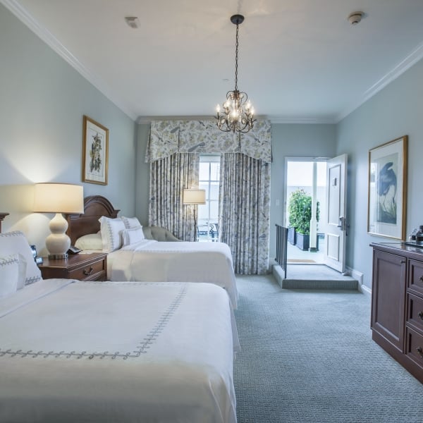 Hotel room with two double beds, dark wood furniture, and an open door leading to an outdoor sundeck.