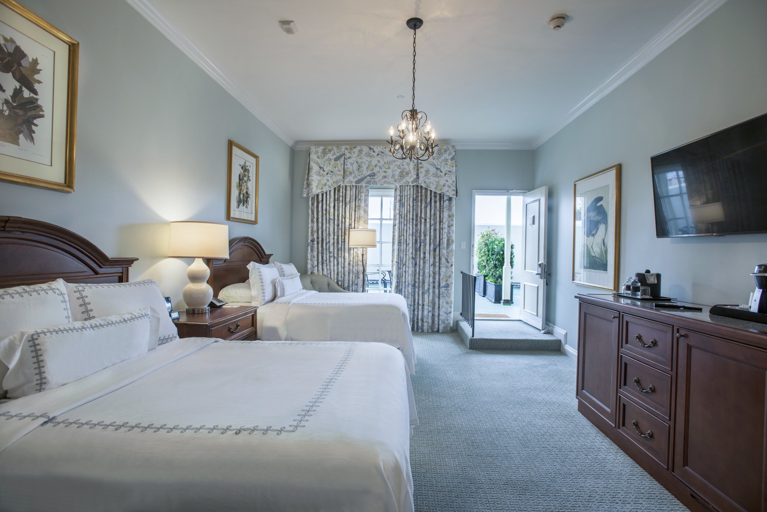Hotel room with two double beds, dark wood furniture, and an open door leading to an outdoor sundeck.