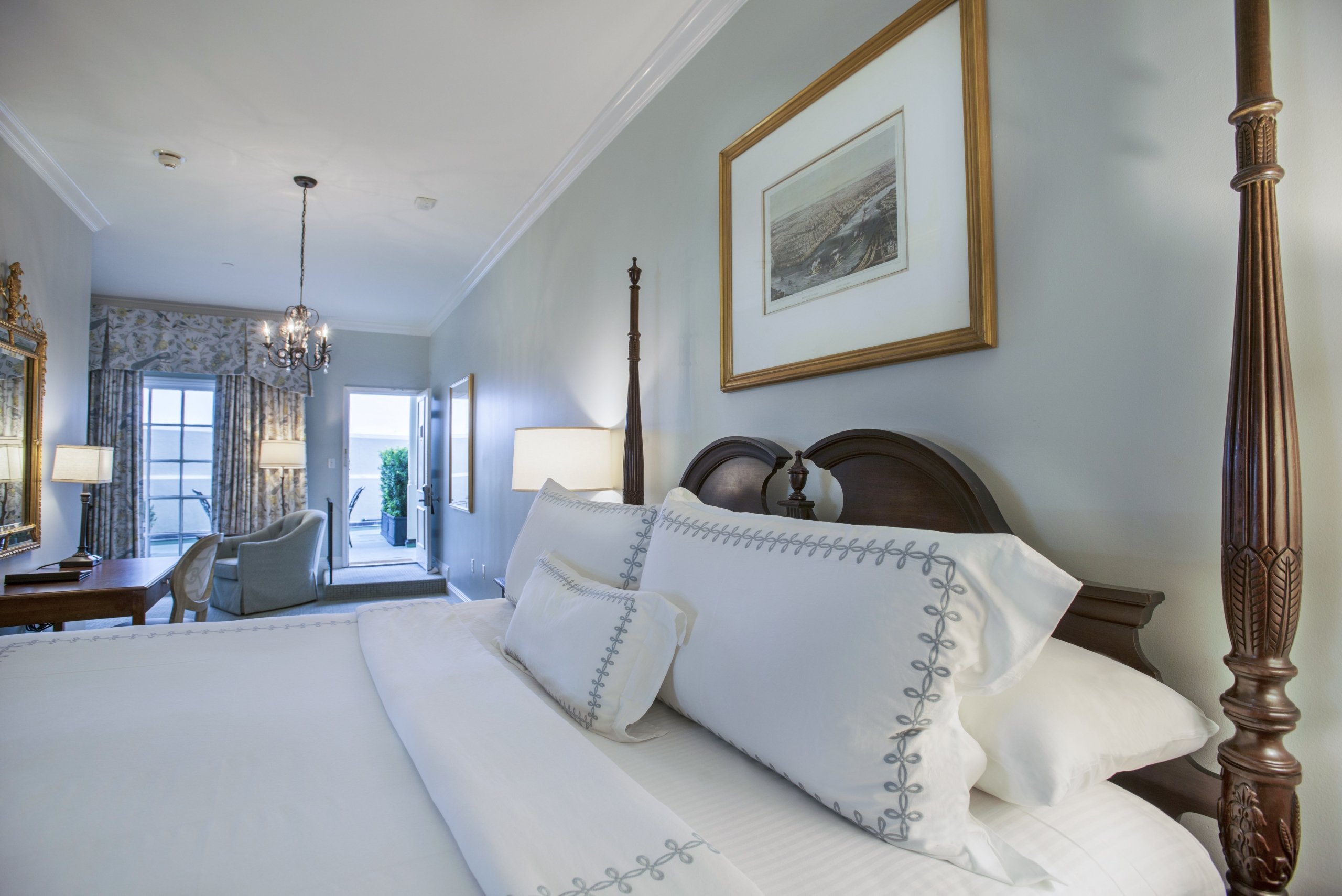 SunDeck King room with a four-poster bed and white linens, a writing desk, and an open glass door leading out to the sundeck.
