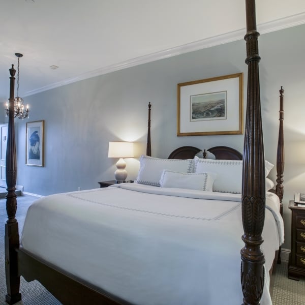 Full view of the SunDeck King room with a four-poster bed, nightstands, and a seating area visible through a doorway to the sun deck.