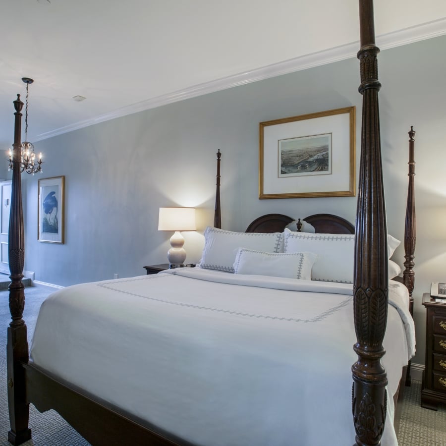 Full view of the SunDeck King room with a four-poster bed, nightstands, and a seating area visible through a doorway to the sun deck.