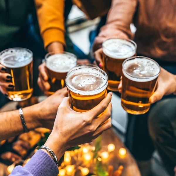 Group of friends drinking and toasting glass of beer at brewery pub restaurant- Happy multiracial people enjoying happy hour with pint sitting at bar table- Youth Food and beverage lifestyle concept