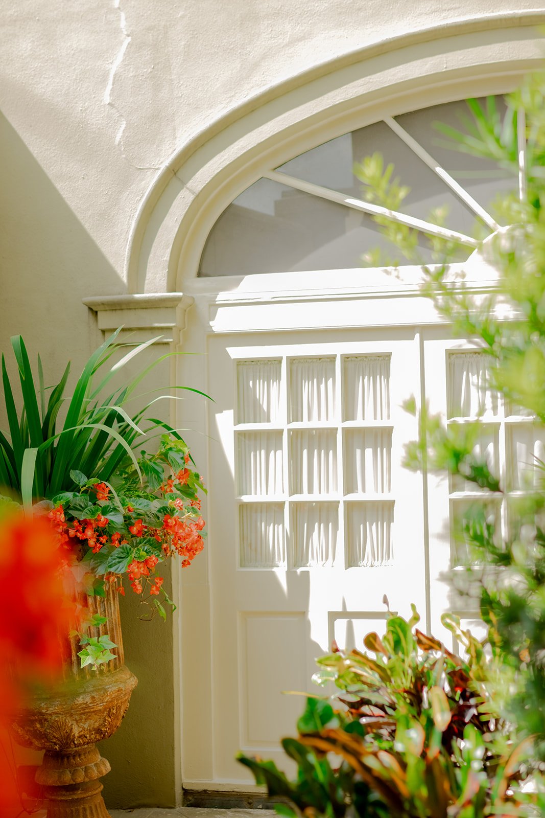 A close-up of a white arched window and doorway, framed by a large planter with bright orange flowers.
