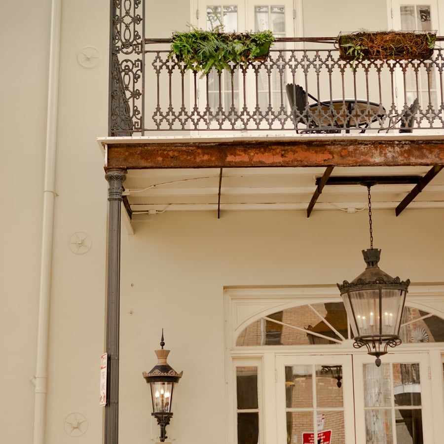 A close-up of the Bienville House exterior showing a wrought-iron balcony, gas lantern, and brass hotel sign.