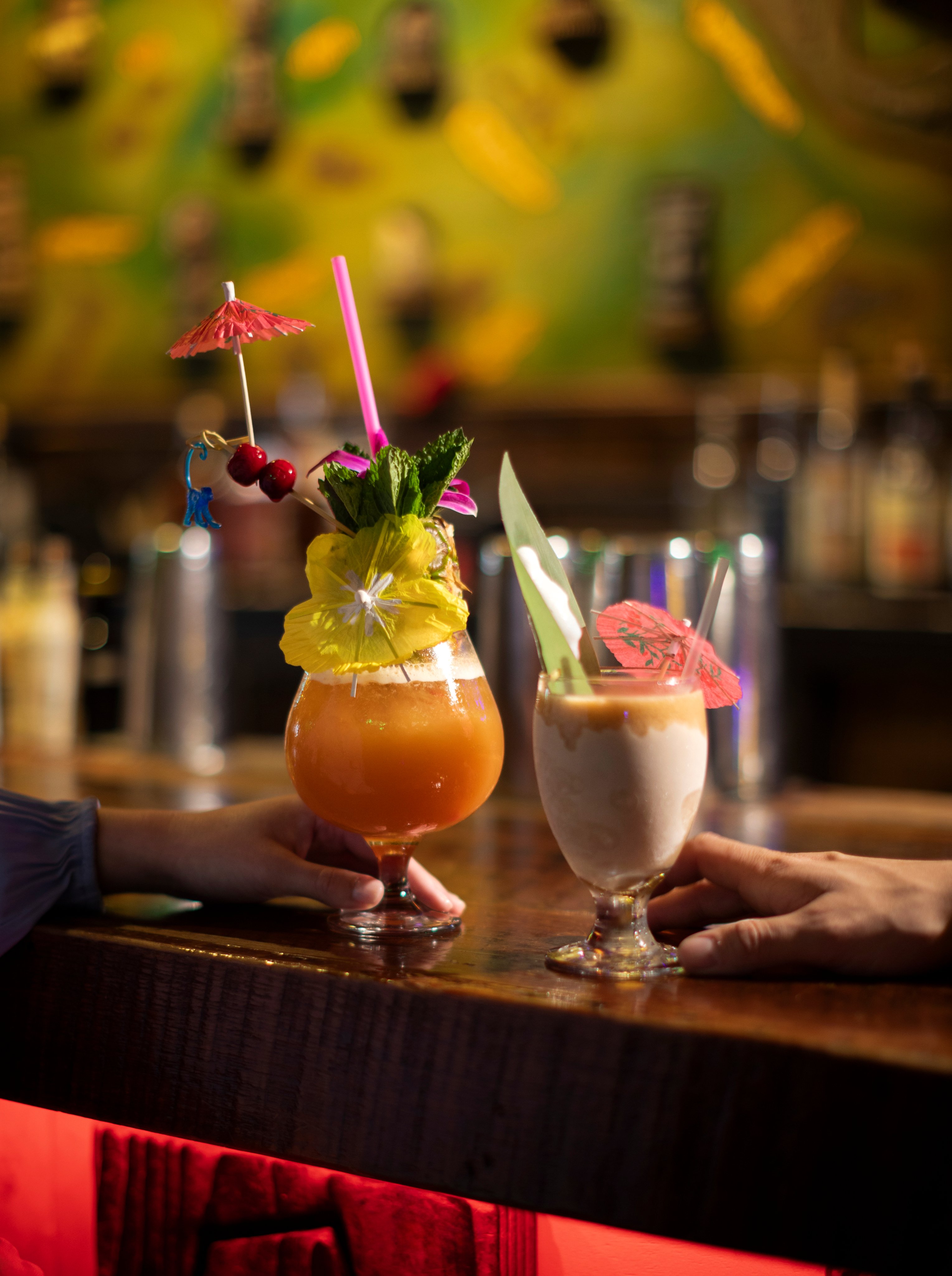 Two colorful cocktails with umbrellas and garnishes on a bar