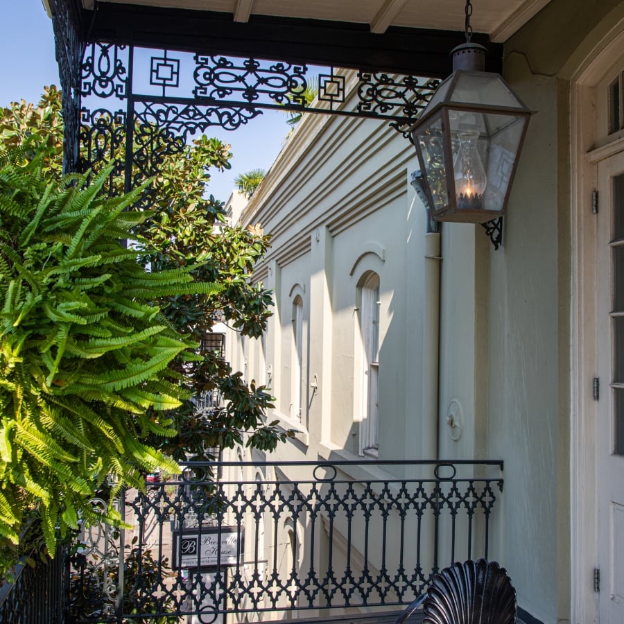 A private wrought-iron balcony with a small table, chair, and hanging lantern at the Bienville House Hotel.