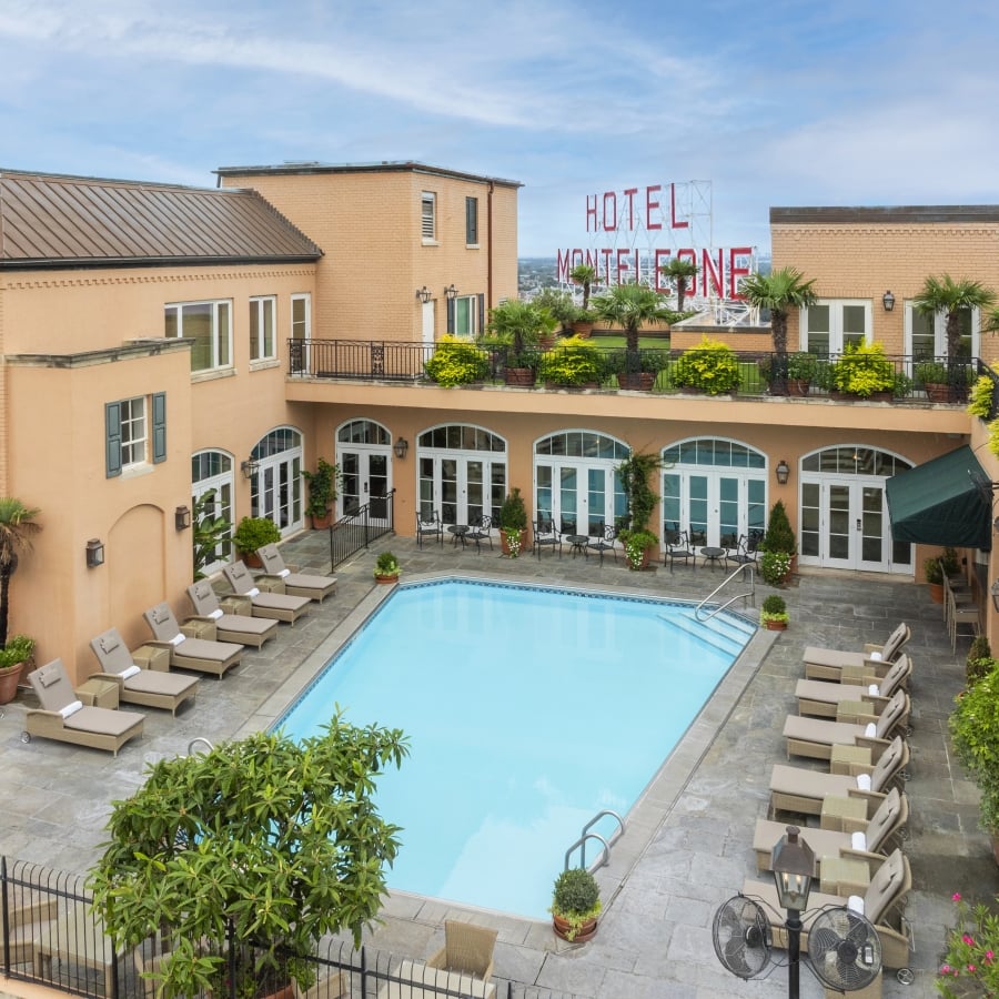 Aerial view of the Hotel Monteleone rooftop pool deck and surrounding peach-colored brick buildings with a large sign in the distance.
